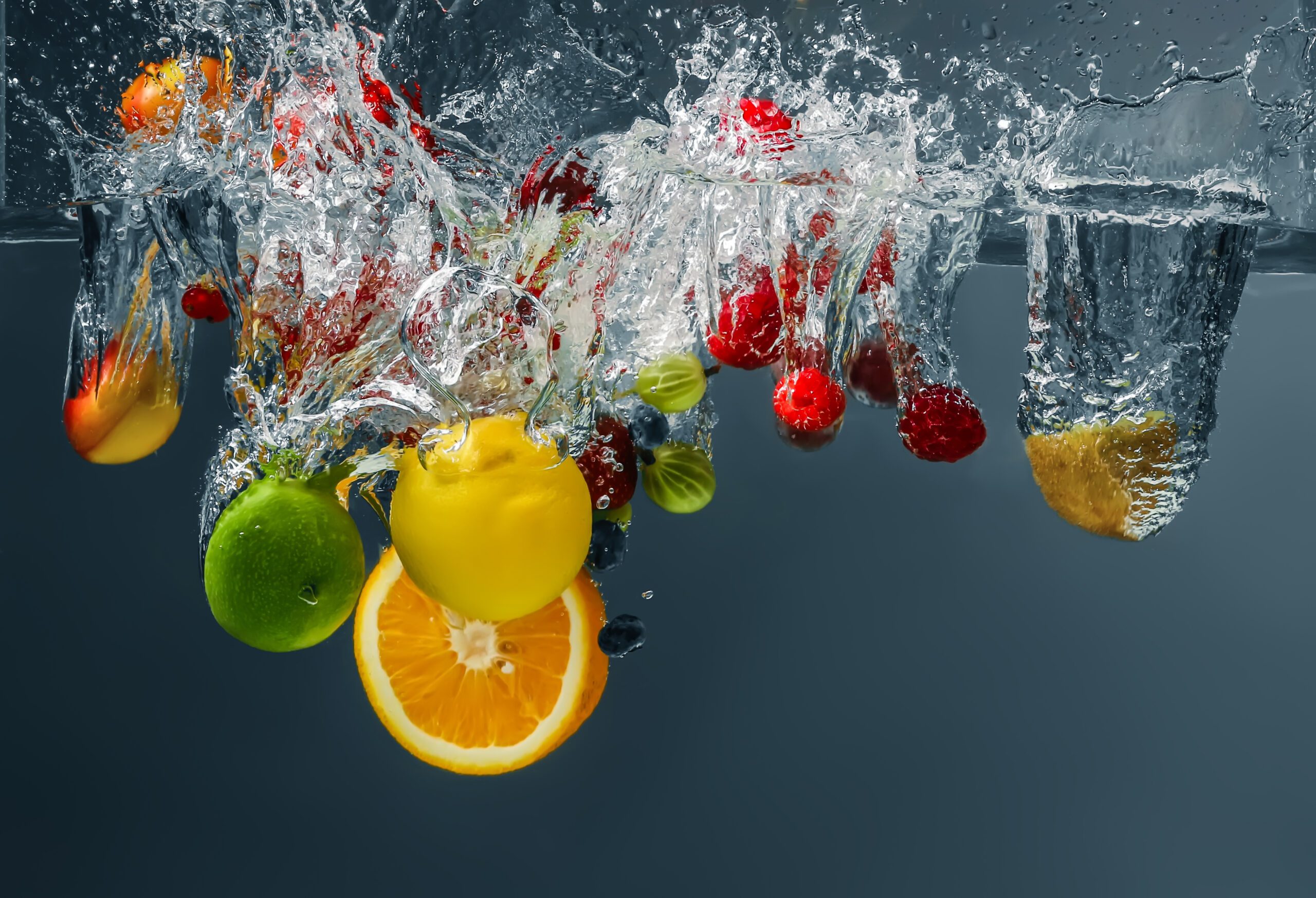 Different fruits and berries falling in water on dark background